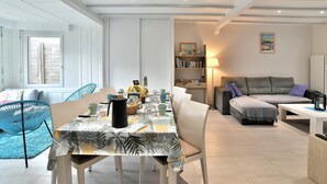 A modern living room with a dining area, featuring a sofa, a coffee table, and a bookshelf.