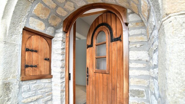 A stone archway leading to a wooden door with a glass panel and a smaller door to the left.