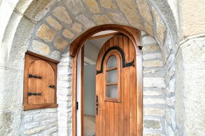 Un arco de piedra que da paso a una puerta de madera con un panel de vidrio y otra puerta más pequeña a la izquierda.