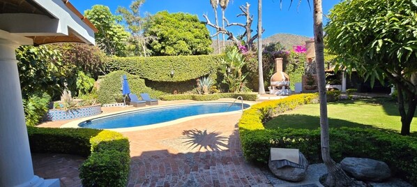 Área de piscina com um caminho de tijolos, um mostrador solar e um forno de barro.