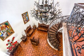 Una escalera de caracol con barandilla de hierro forjado, un candelabro y suelo de baldosas.