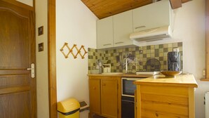 A compact kitchen with wooden cabinets, a built-in oven, a coffee maker, and a trash bin. - Studio Avec Véranda Dans Vallée Calme à Reynès (Reynes)