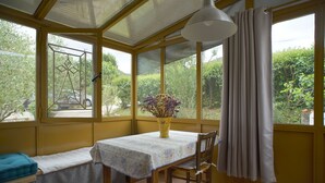 A conservatory with a table and chair, a bench, and a vase with flowers. - Studio Avec Véranda Dans Vallée Calme à Reynès (Reynes)