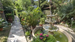 Ein Garten mit einem Kiesweg, einer mehrstufigen Fontäne und unterschiedlichen Pflanzen.