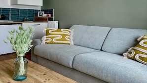 Uma sala de estar moderna com um sofá cinza, uma mesa de centro de madeira e um vaso com plantas verdes.