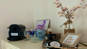 Uma bancada de cozinha com cafeteira, potes, um quadro emoldurado, uma vela e uma placa decorativa.