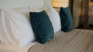 Un lit avec des oreillers blancs et turquoise, une couvre-lit beige matelassée et une tête de lit en bois.