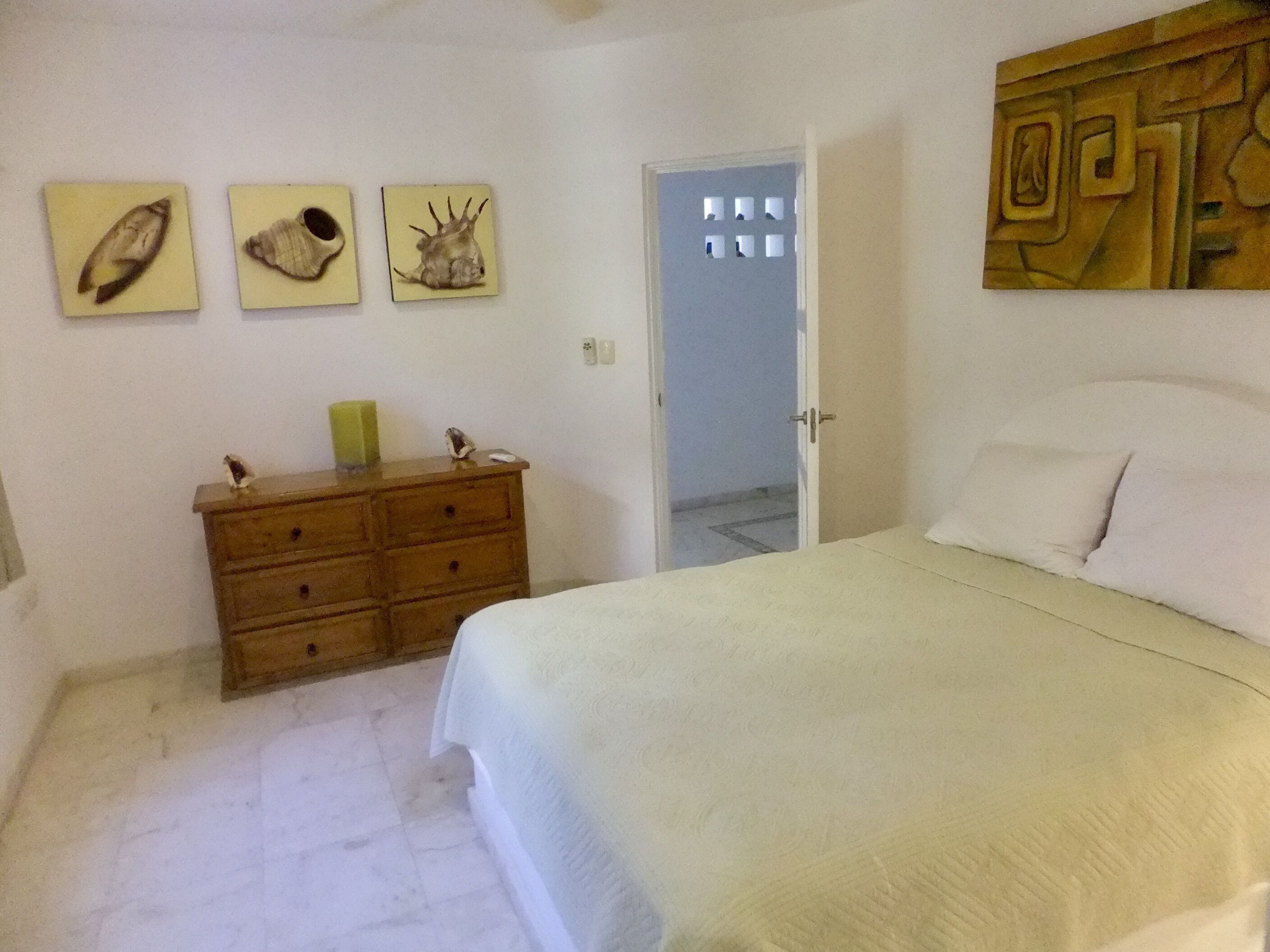 A bedroom with a bed, a wooden dresser, and three wall-mounted pictures.