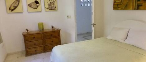 A bedroom with a bed, a wooden dresser, and three wall-mounted pictures.