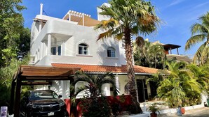 A white building with a red-tiled roof, a covered carport, and a palm tree in the foreground. - Christmas Deal!Oceanview private pool villa, steps from the beach. 24hs security (Playa del Carmen)