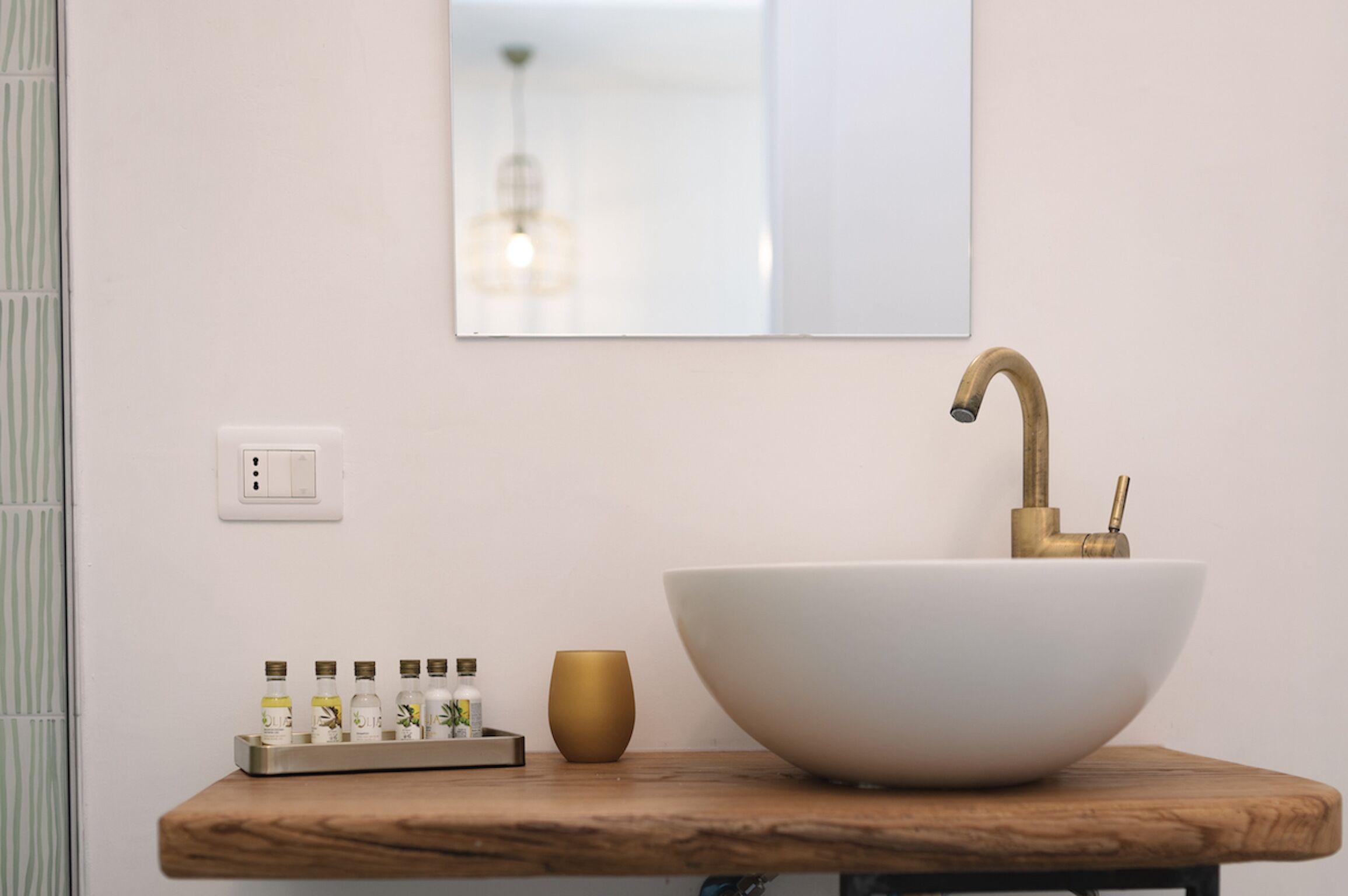 A bathroom with a large white vessel sink, a gold faucet, a wooden countertop, and a mirror above the sink.