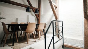 A dining area with a wooden table and chairs, a black pendant light, and exposed wooden beams. - Guldgränd  (Stockholm)