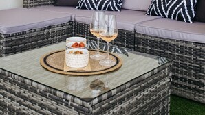 A wicker sofa with cushions, a round coffee table with a glass of wine, and a bowl of snacks. - Modern and cosy apartment with a beautiful terrace and parking, Paris La Défense (Courbevoie)