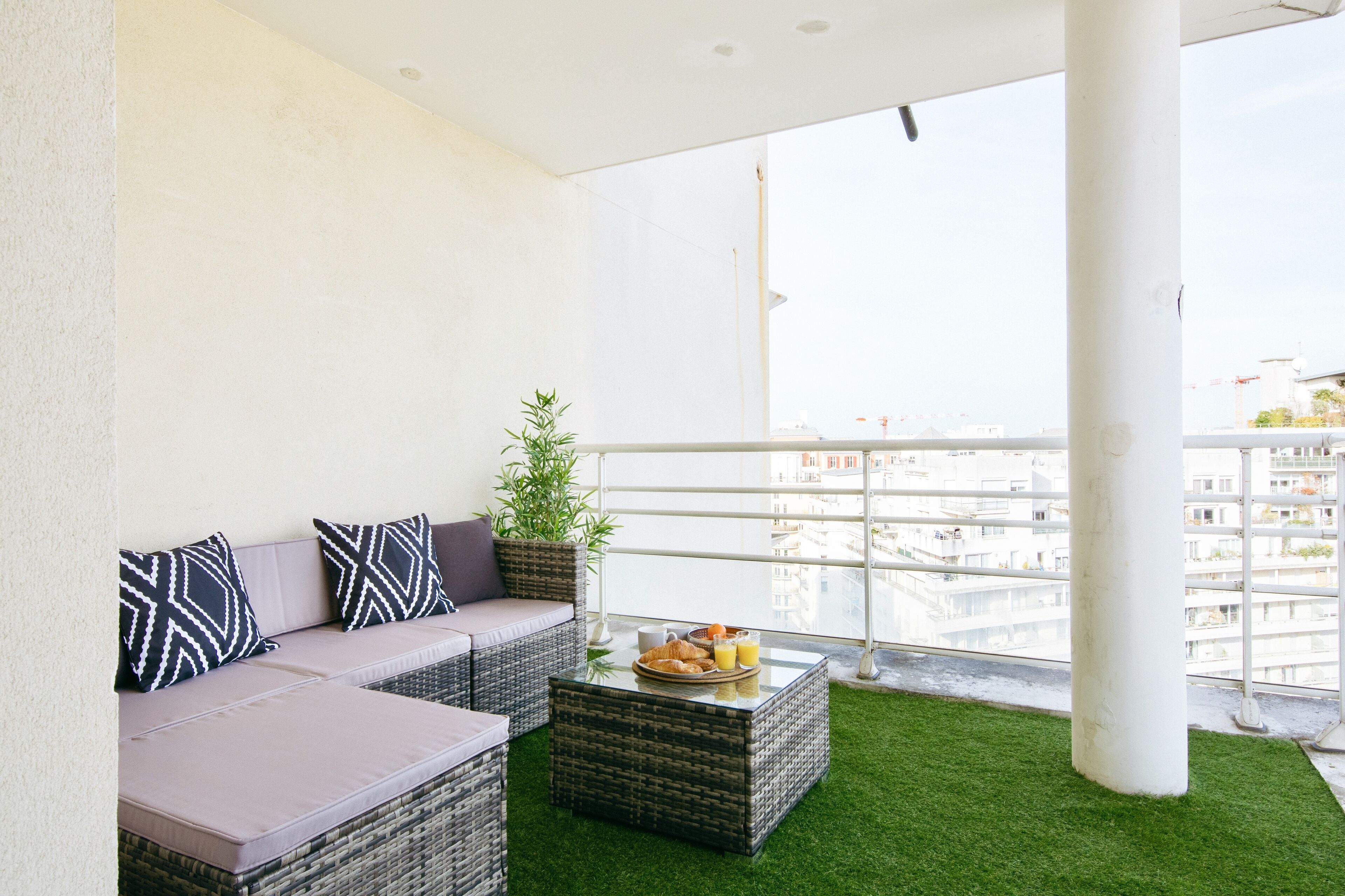 A balcony with a wicker sofa, a small table with fruits and juice, and a potted plant.