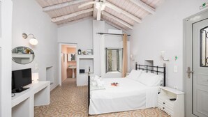 A bedroom with a bed, a TV, a desk, a mirror, a bathroom, and a window. - Aimilia Cottage - One Bedroom Apartment, Sleeps 2 (Longos)
