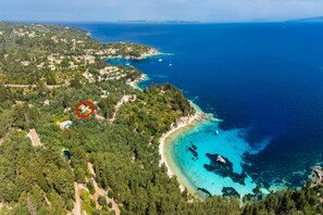 Vista aérea de una zona costera con playa, aguas cristalinas y una propiedad delimitada rodeada de vegetación.