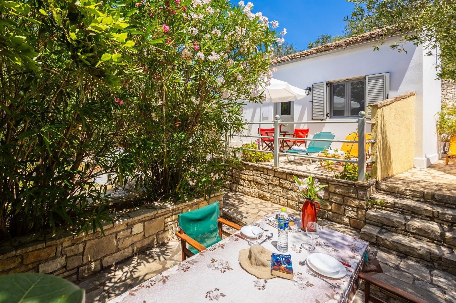 An outdoor dining area with a table set for two, surrounded by stone walls and a white building with shutters.