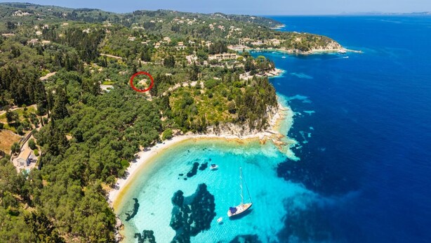 An aerial view of a coastal area with a beach, clear blue waters, and a small island with a red circle marking a specific location. - Eleni Cottage - One Bedroom Apartment, Sleeps 2 (Paxi)