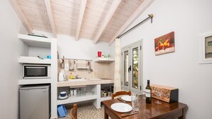 Cocina compacta con microondas, fregadero y refrigerador pequeño. Hay una mesa de comedor con sillas y una botella de vino.