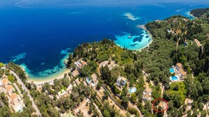 Vista aérea de una zona costera con aguas azul turquesa, una playa y edificios residenciales rodeados de vegetación.