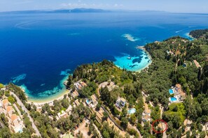 Vue aérienne d’une zone côtière avec des eaux d’un bleu limpide, une plage et des immeubles résidentiels entourés de verdure.