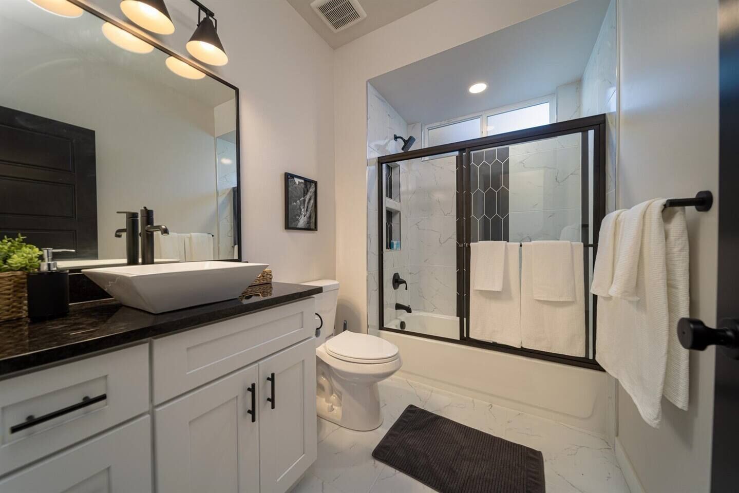 A modern bathroom with a large mirror, a white sink, a toilet, and a glass-enclosed shower.