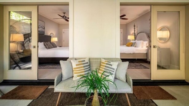 Ein Hotelzimmer mit zwei Betten, einem Schlafsofa, einem Deckenventilator und einer Zimmerpflanze.
