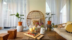 A cozy room with a round wicker chair, a wooden coffee table with a tray of snacks, and two potted plants.