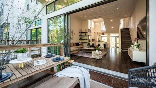 A modern interior with a wooden deck, a dining area with a table and chairs, and a staircase leading to an upper level.