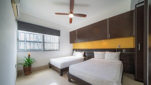 Une chambre d’hôtel avec deux lits, un ventilateur de plafond, une fenêtre avec des stores et une plante en pot.