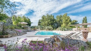Un espace piscine avec une eau d’un bleu limpide, entouré de murs en pierre et d’une végétation luxuriante.