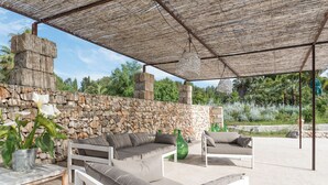 Un espace extérieur aménagé avec un mur en pierre, une terrasse couverte et une vue sur le paysage environnant.