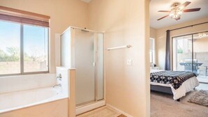 Een badkamer met een bad, douche en glazen deur die naar een slaapkamer leidt.