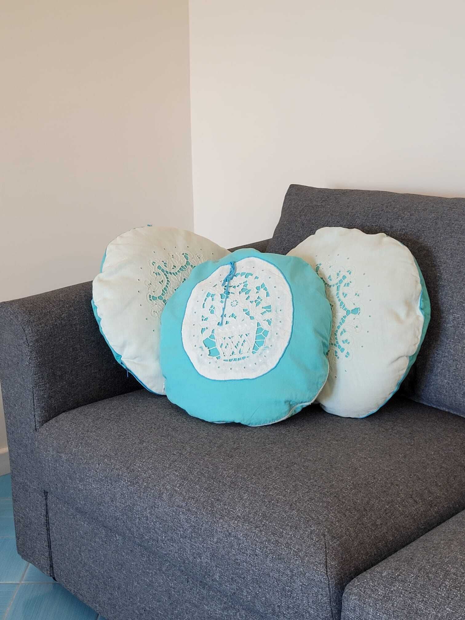 A grey sofa with three decorative pillows, one with a blue and white pattern, and two plain white pillows.