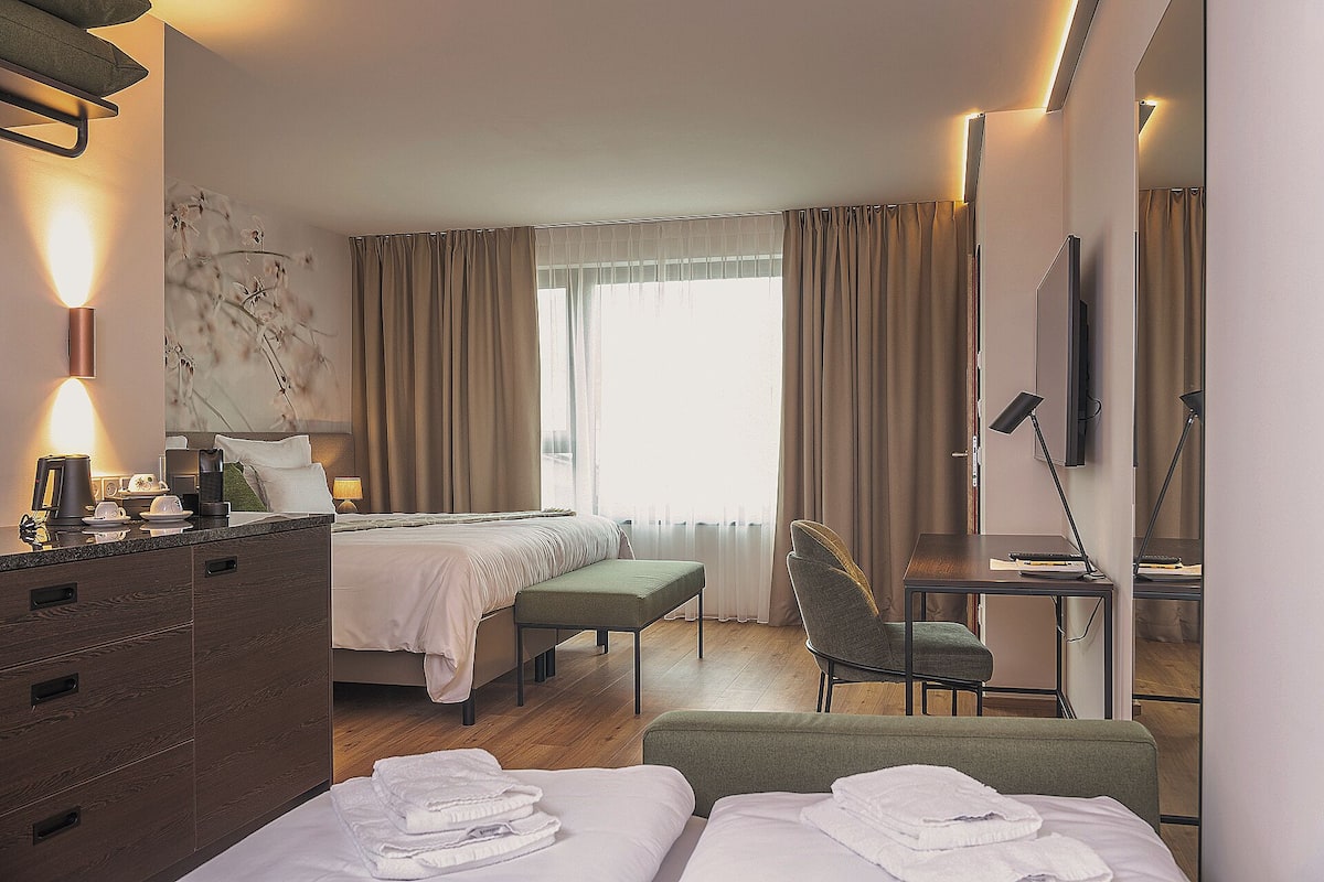 A hotel room with a bed, a desk, a chair, a TV, and a lamp.