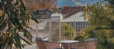 Eine Terrasse mit Korbstühlen und einem Tisch, mit Blick auf einen Kirchturm und eine gebirgige Landschaft.