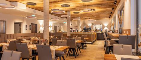 A modern restaurant with wooden flooring, round ceiling lights, and a bar area.