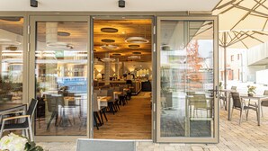 Un restaurante moderno con entrada de vidrio, techo de madera y varias mesas y sillas.