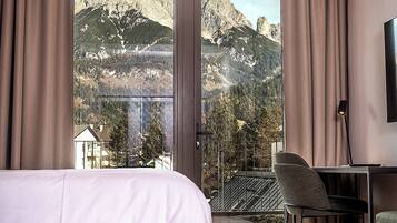 Ein Hotelzimmer mit Bett, Schreibtisch, Stuhl und großem Fenster mit Blick auf die Berge.