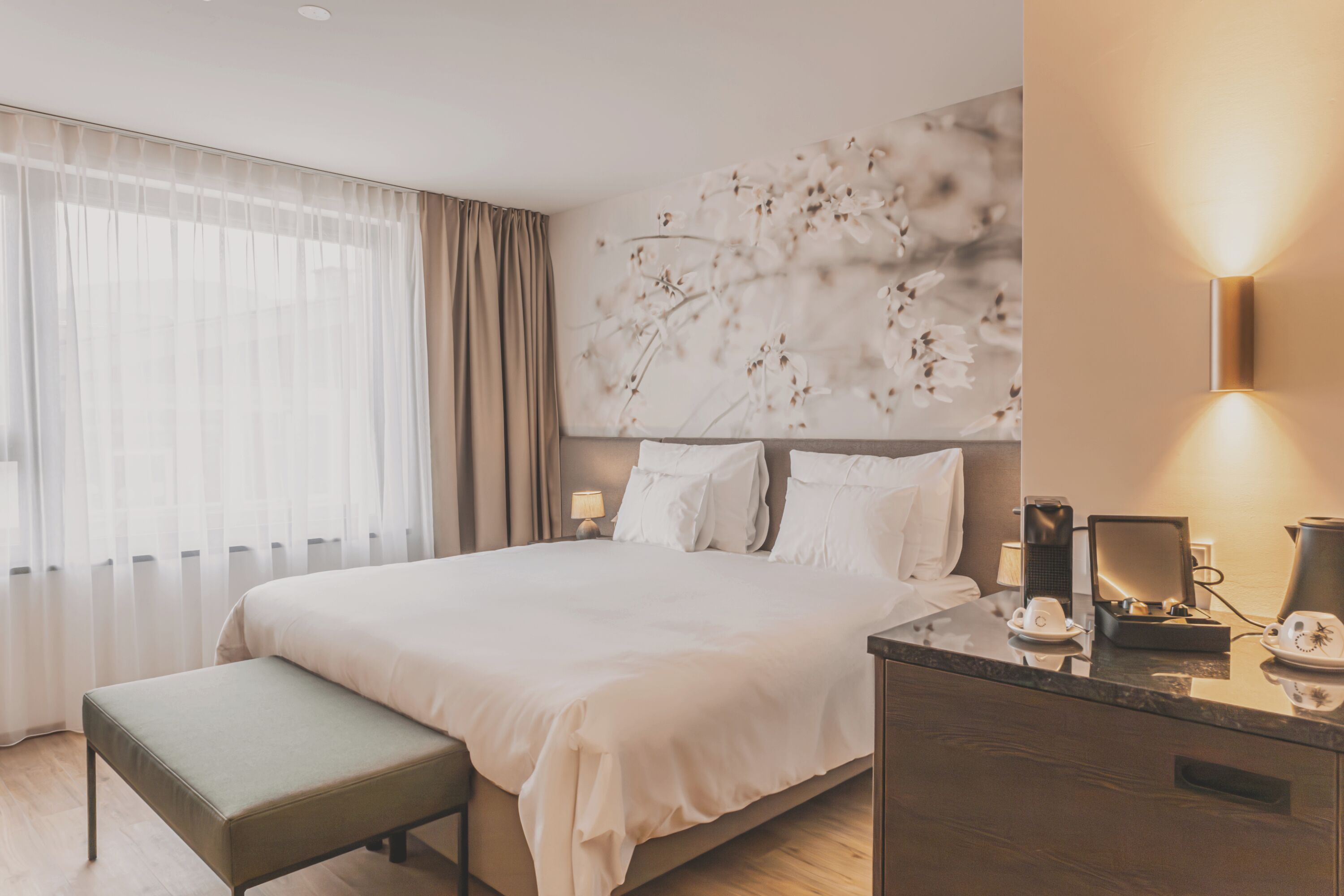 A modern hotel room with a large bed, a bedside table with a lamp, and a decorative wall piece.