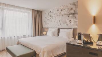 A modern hotel room with a large bed, a bedside table with a lamp, and a decorative wall piece.