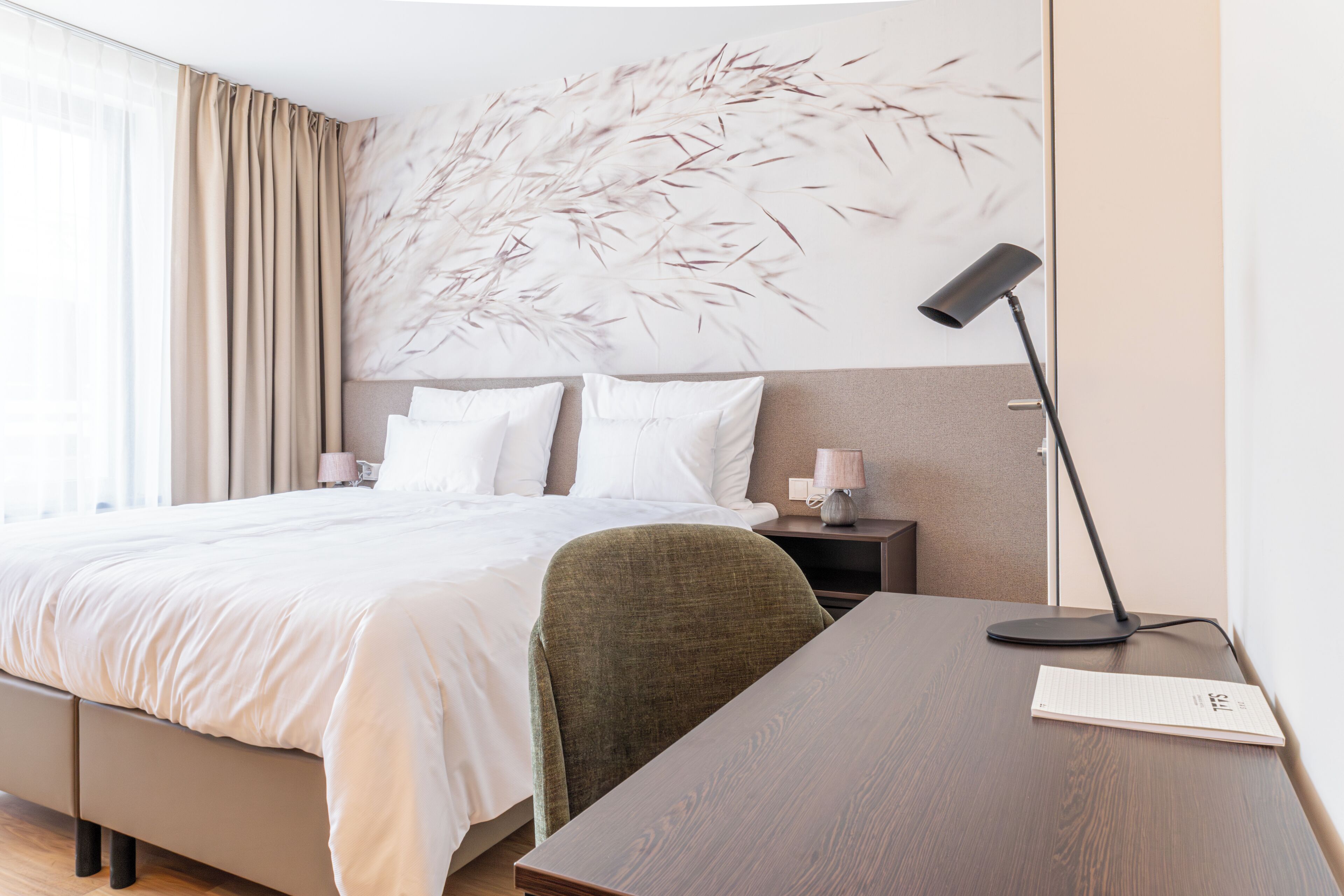 A hotel room with a large bed, a desk, a chair, a lamp, and a wall art piece.