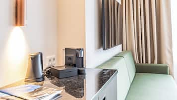 Ein modernes Hotelzimmer mit flachbildfernseher an der Wand, einer Couch, einer Kaffeemaschine und einer Arbeitsplatte mit einer Zeitschrift.