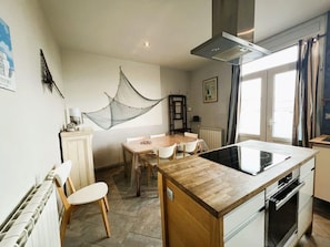 A kitchen with a central island, a dining table, chairs, a radiator, and a hanging net.