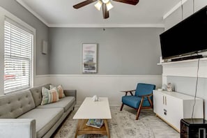 A living room with a sofa, a coffee table, a blue chair, a TV, and a ceiling fan. - Hot Tub - Historic District - Next to Forsyth Park (Savannah)