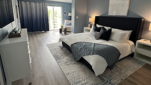 A modern bedroom with a large bed, a ceiling fan, and a view of the outdoors through a sliding door.