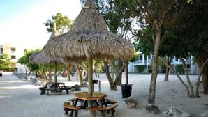 A beachside area with thatched umbrellas and wooden picnic tables.