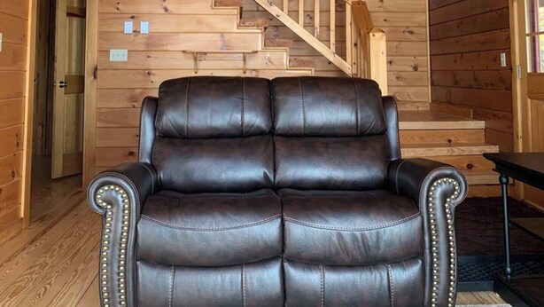 Ein Holzblockhaus-Interieur mit einem Ledersofa, einer Holztreppe und einem großen Fellteppich.