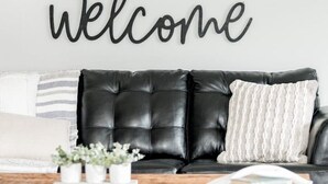 A black leather sofa with a white pillow and a "welcome" sign on the wall.