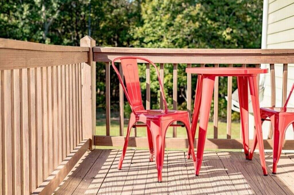 Eine Holzterrasse mit Geländer, roten Plastikstühlen und einem Tisch.